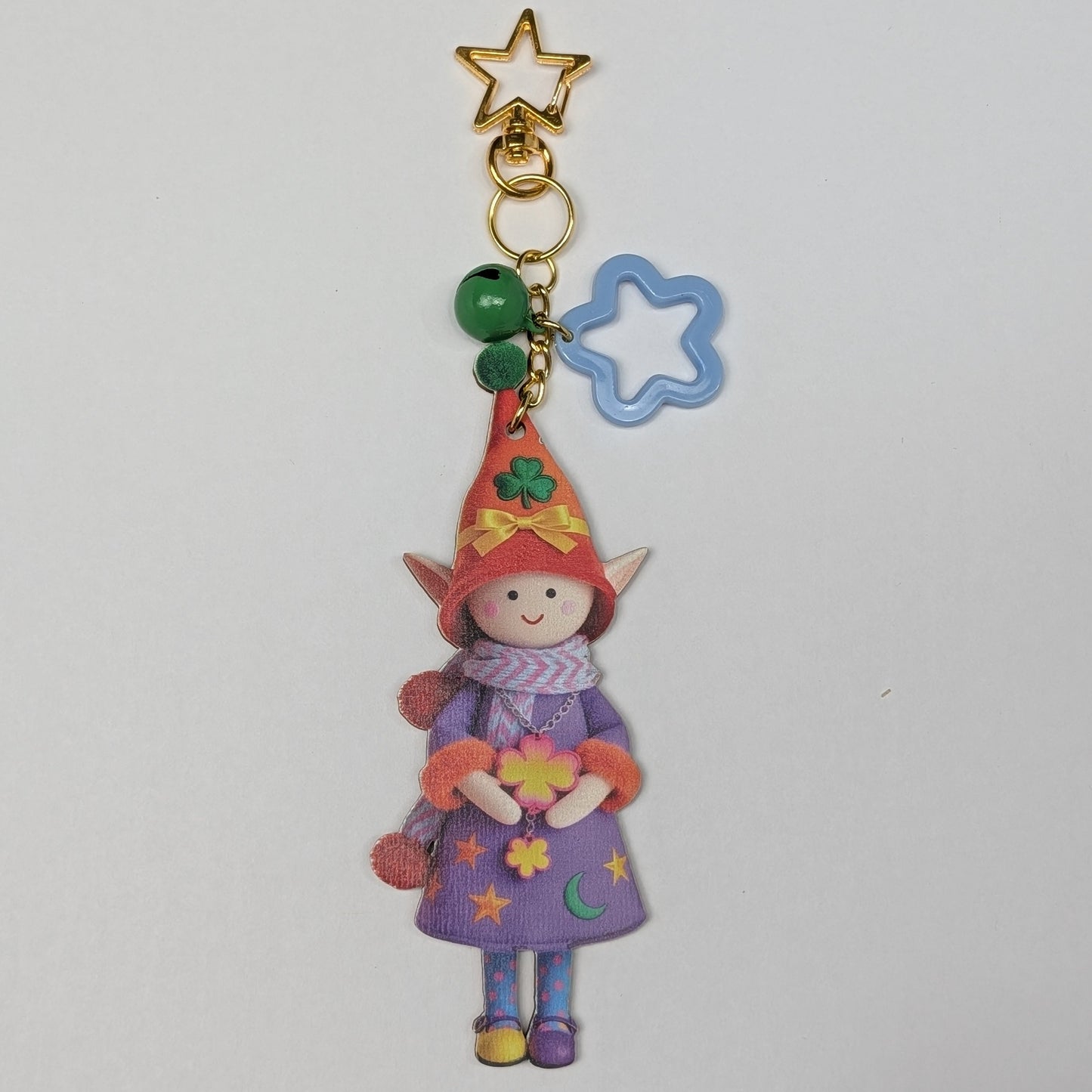 Colorful holiday themed fairy doll keychain with golden star, blue flower, and green bell charm on a white background