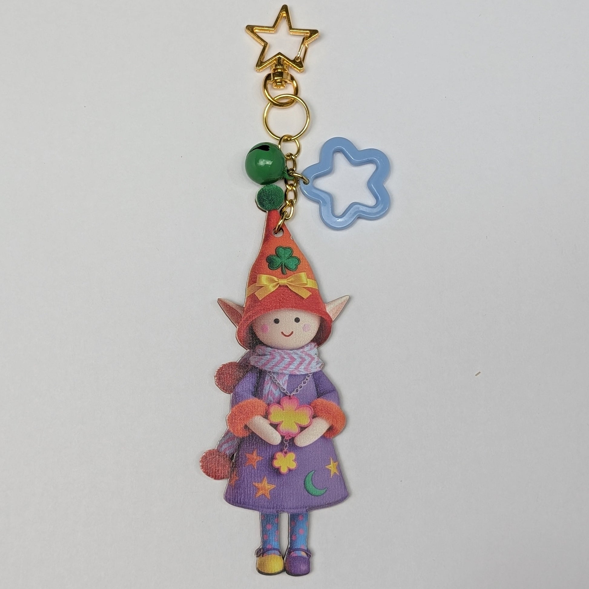 Colorful holiday themed fairy doll keychain with golden star, blue flower, and green bell charm on a white background