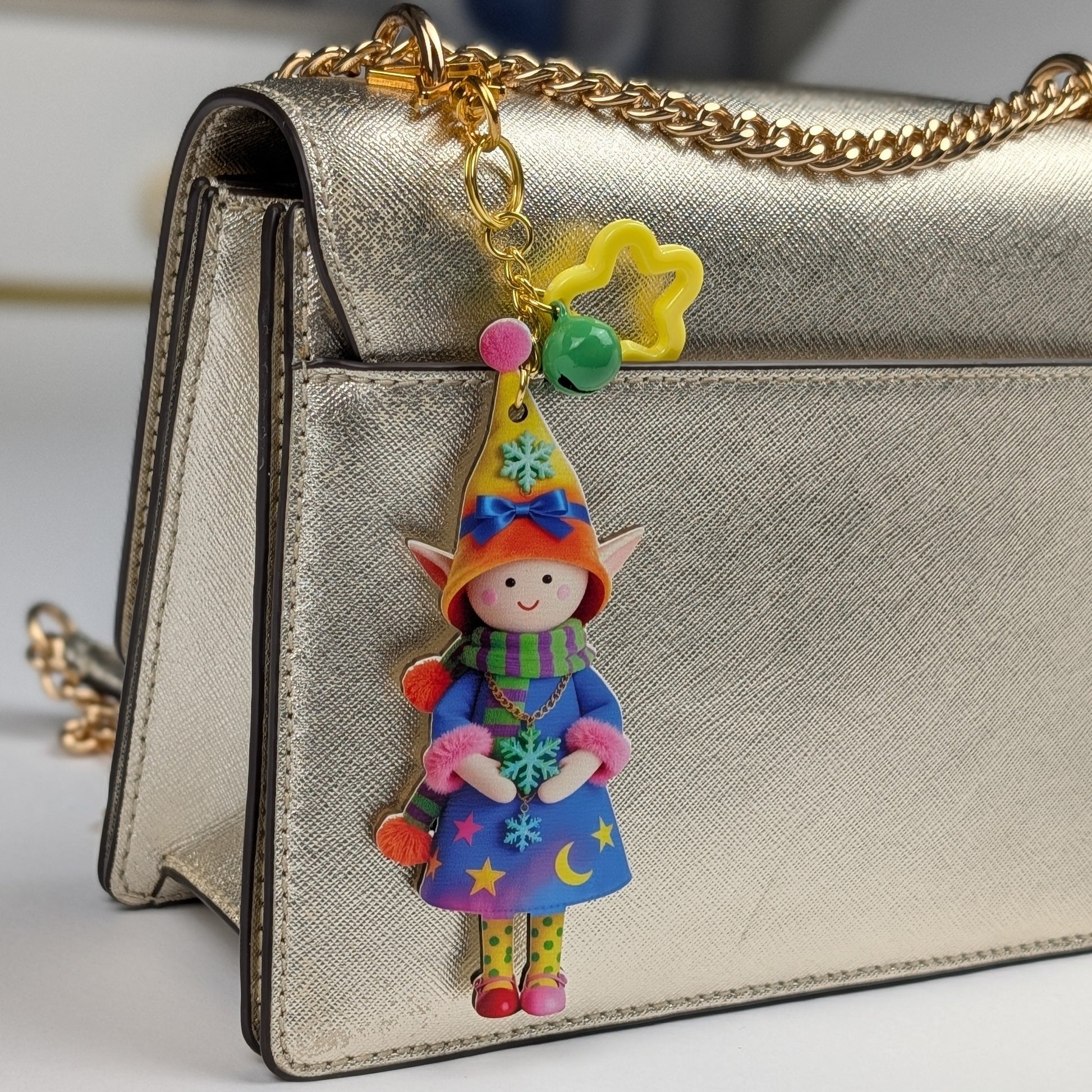 Colorful holiday themed fairy doll keychain with golden star, orange flower, and dark green bell charm attached to a golden women handbag on a light gray background
