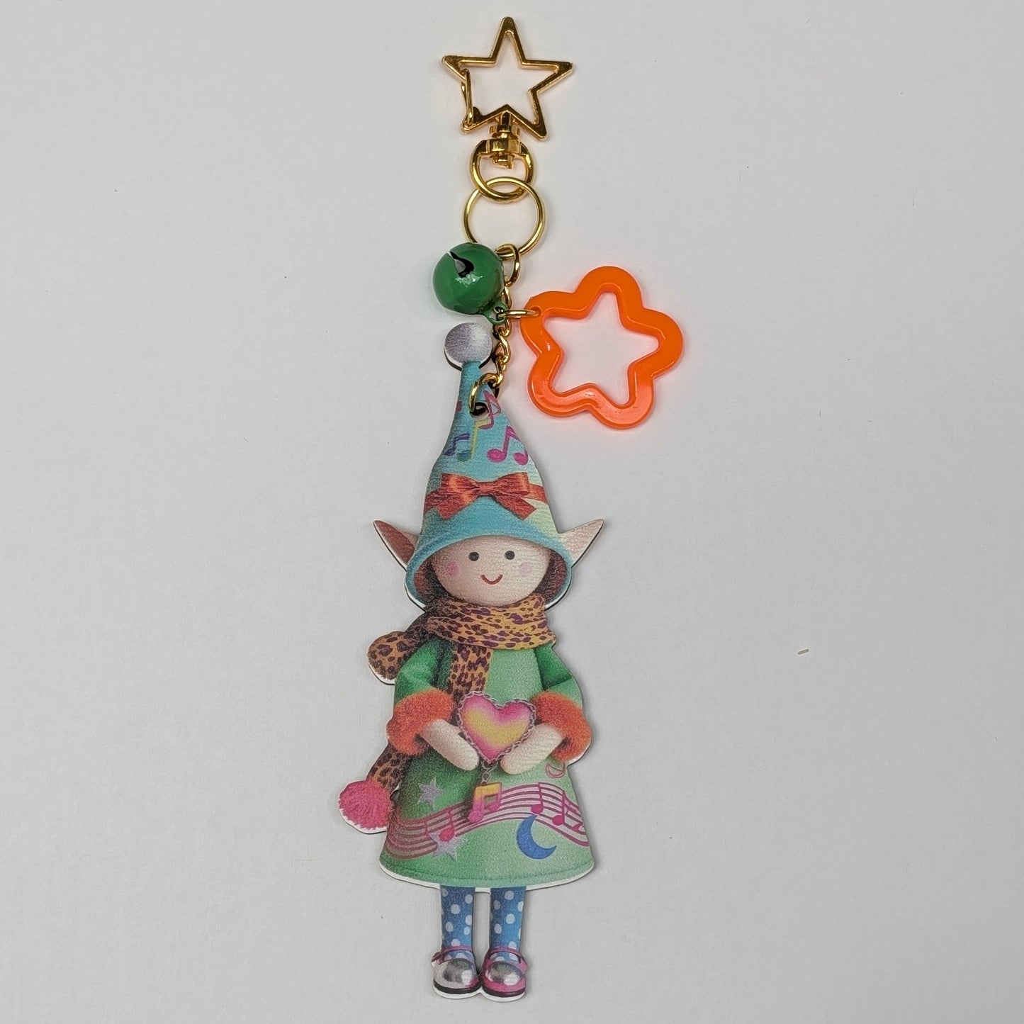 Colorful holiday themed fairy doll keychain with golden star, orange flower, and dark green bell charm on a white background