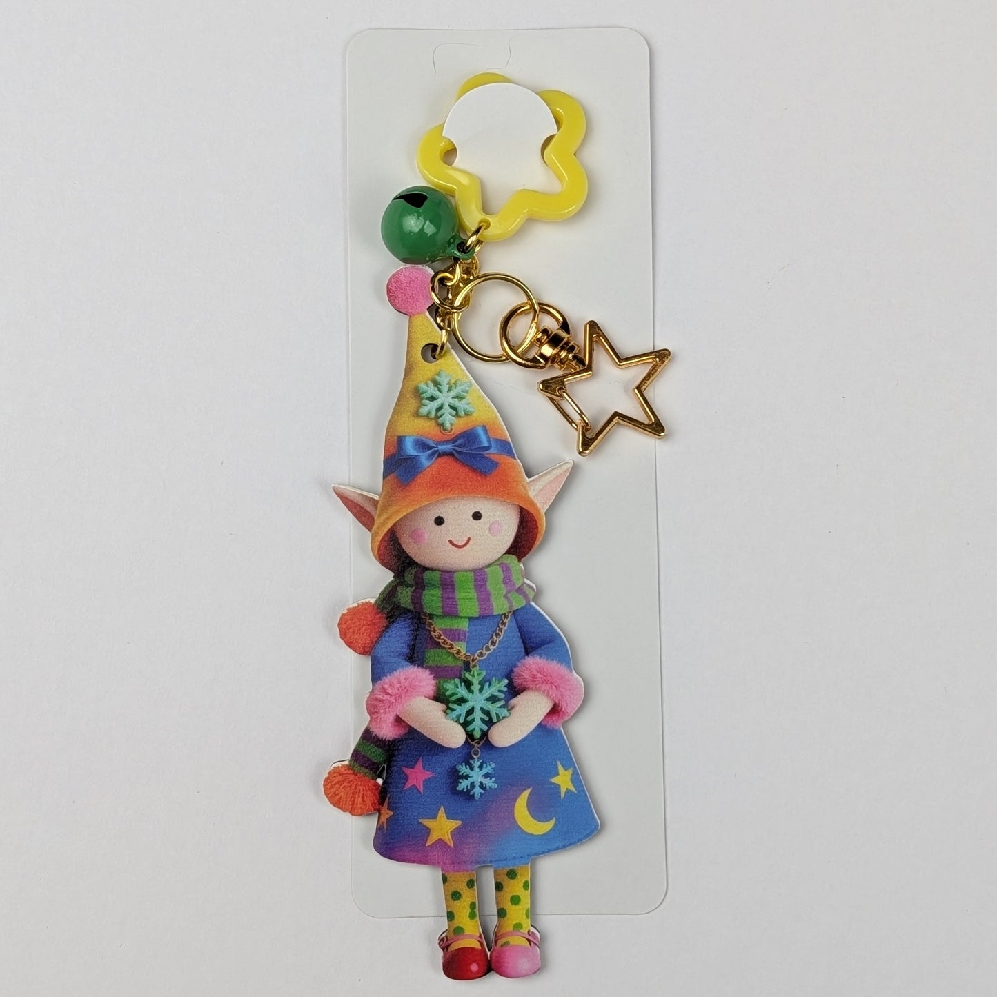 Colorful holiday themed fairy doll keychain with golden star, orange flower, and dark green bell charm white packaging card