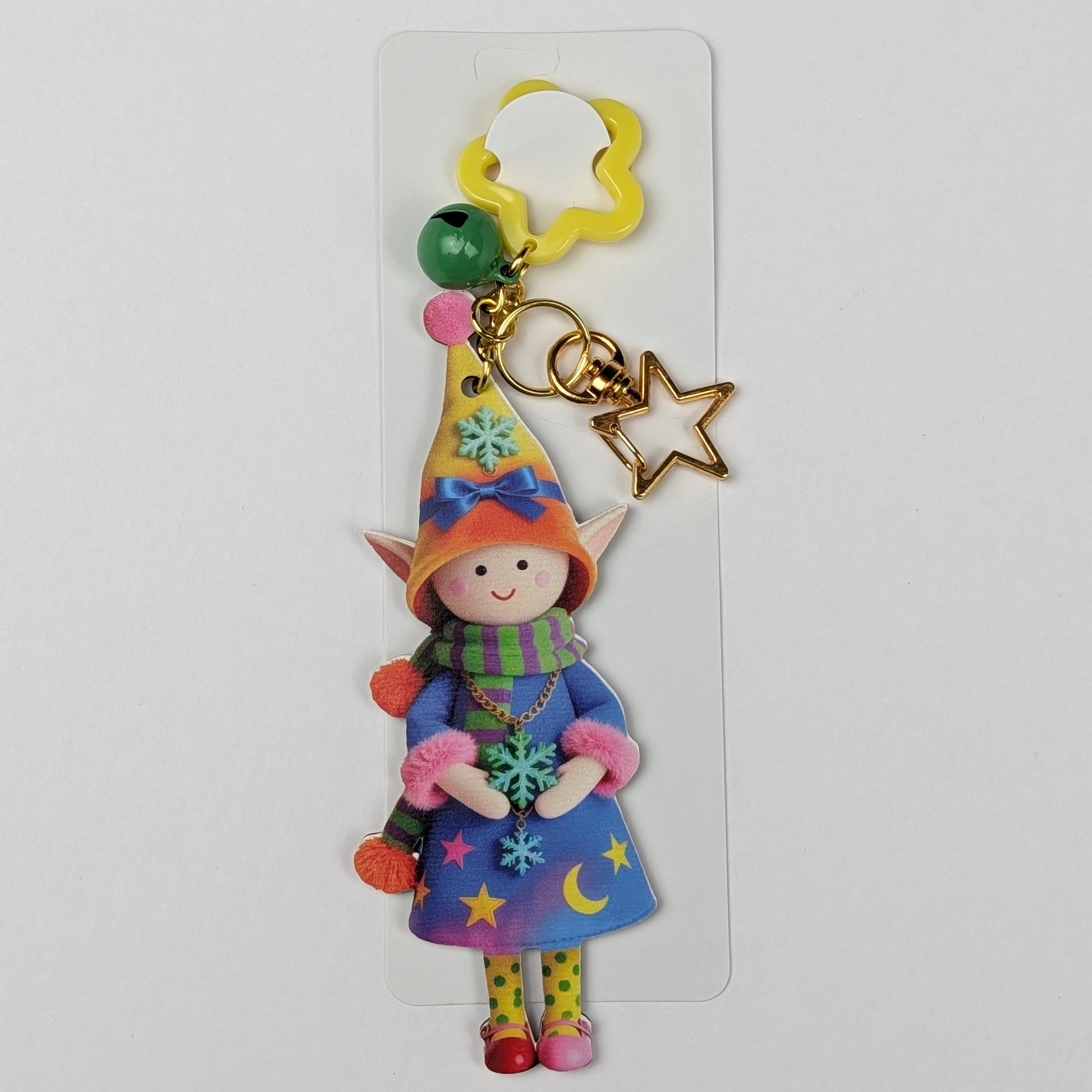 Colorful holiday themed fairy doll keychain with golden star, orange flower, and dark green bell charm white packaging card