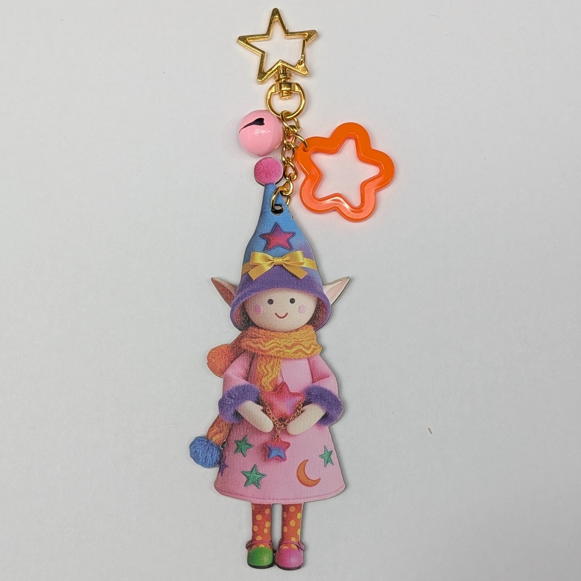 Colorful holiday themed fairy doll keychain with golden star, orange flower, and pink bell charm on a white background