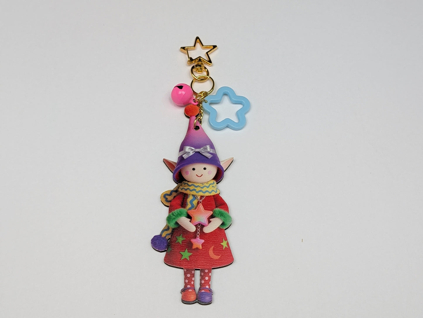 Colorful holiday themed fairy doll keychain with golden star, teal flower, and pink bell charm on a white background