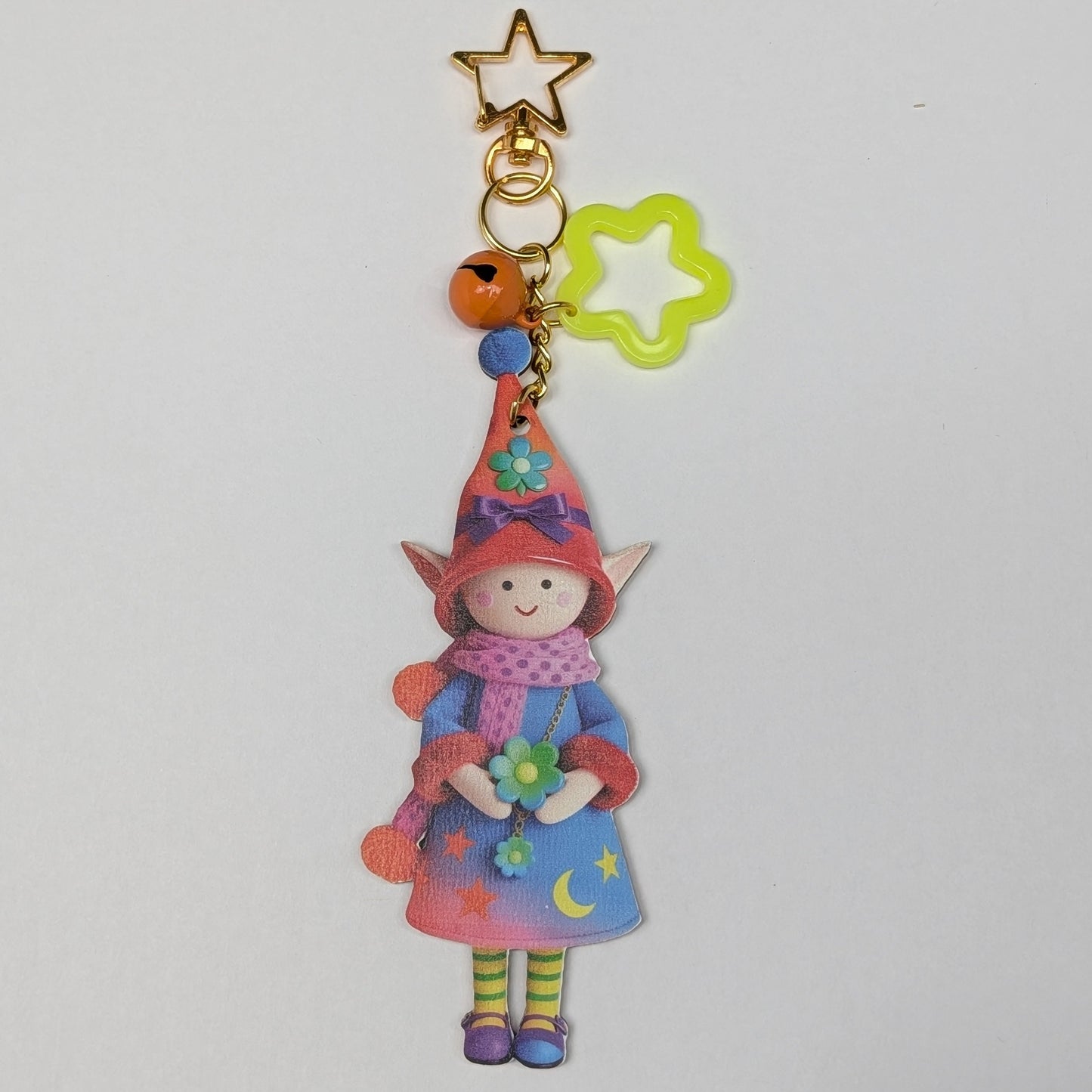 Colorful holiday themed fairy doll keychain with golden star, yellow flower, and orange bell charm on a white background