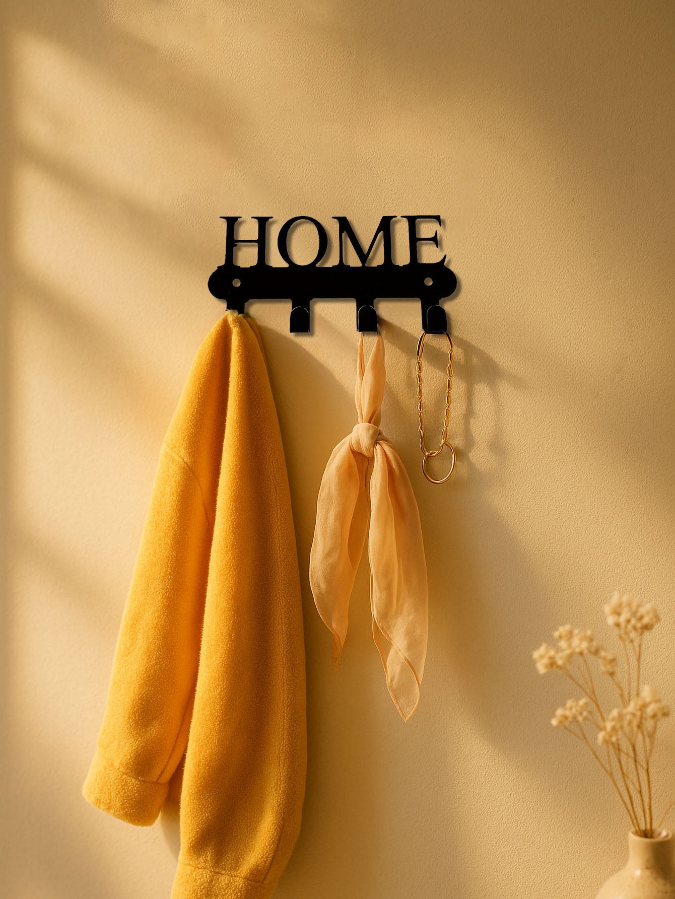 Decorative 4-hook wall mounted key and coat holder rack with 'HOME' text design on a beige wall with yellow and orange items.