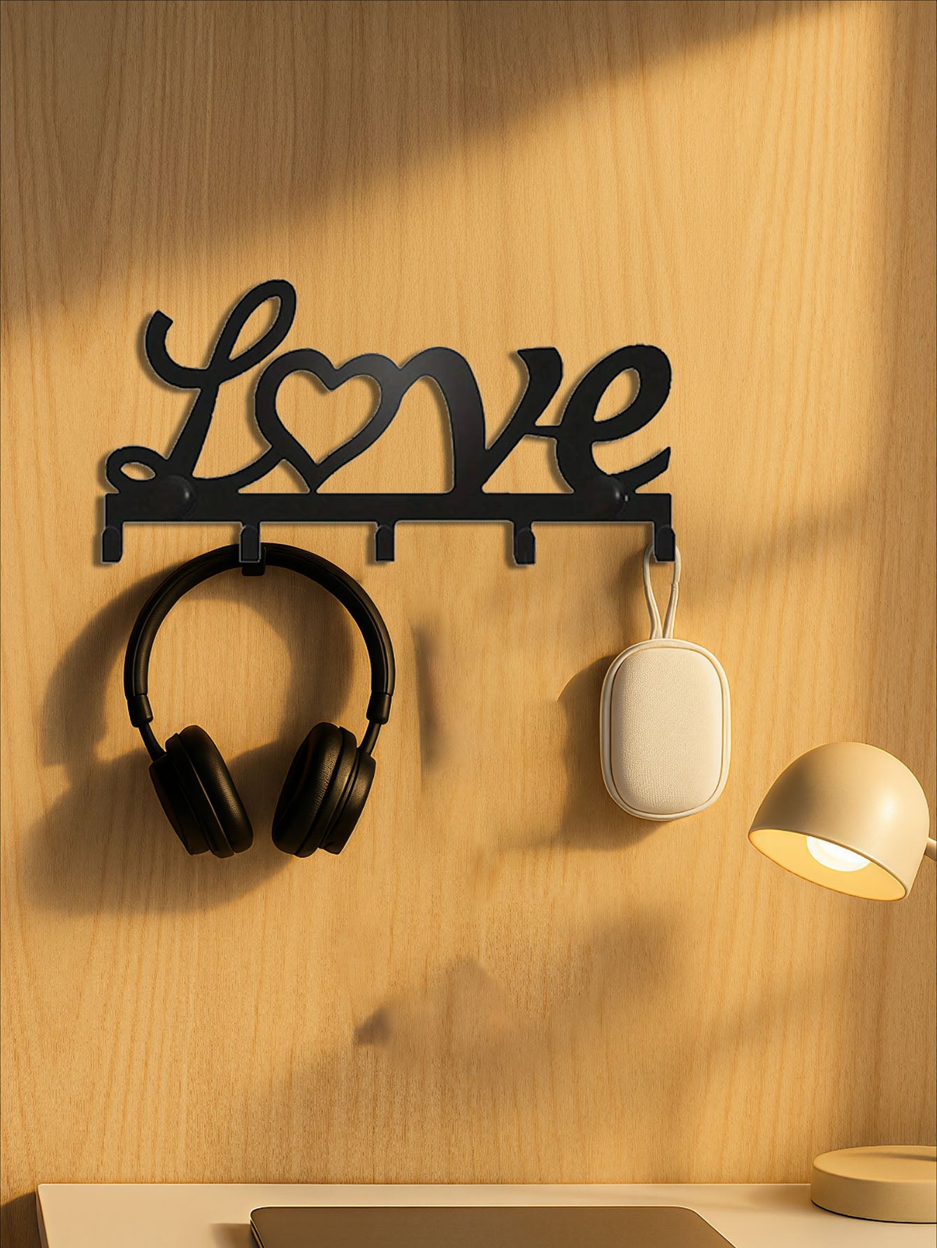 Decorative 5-hook wall mounted key and coat rack with 'love' text design with headphones and a speaker attached on a wooden wall.