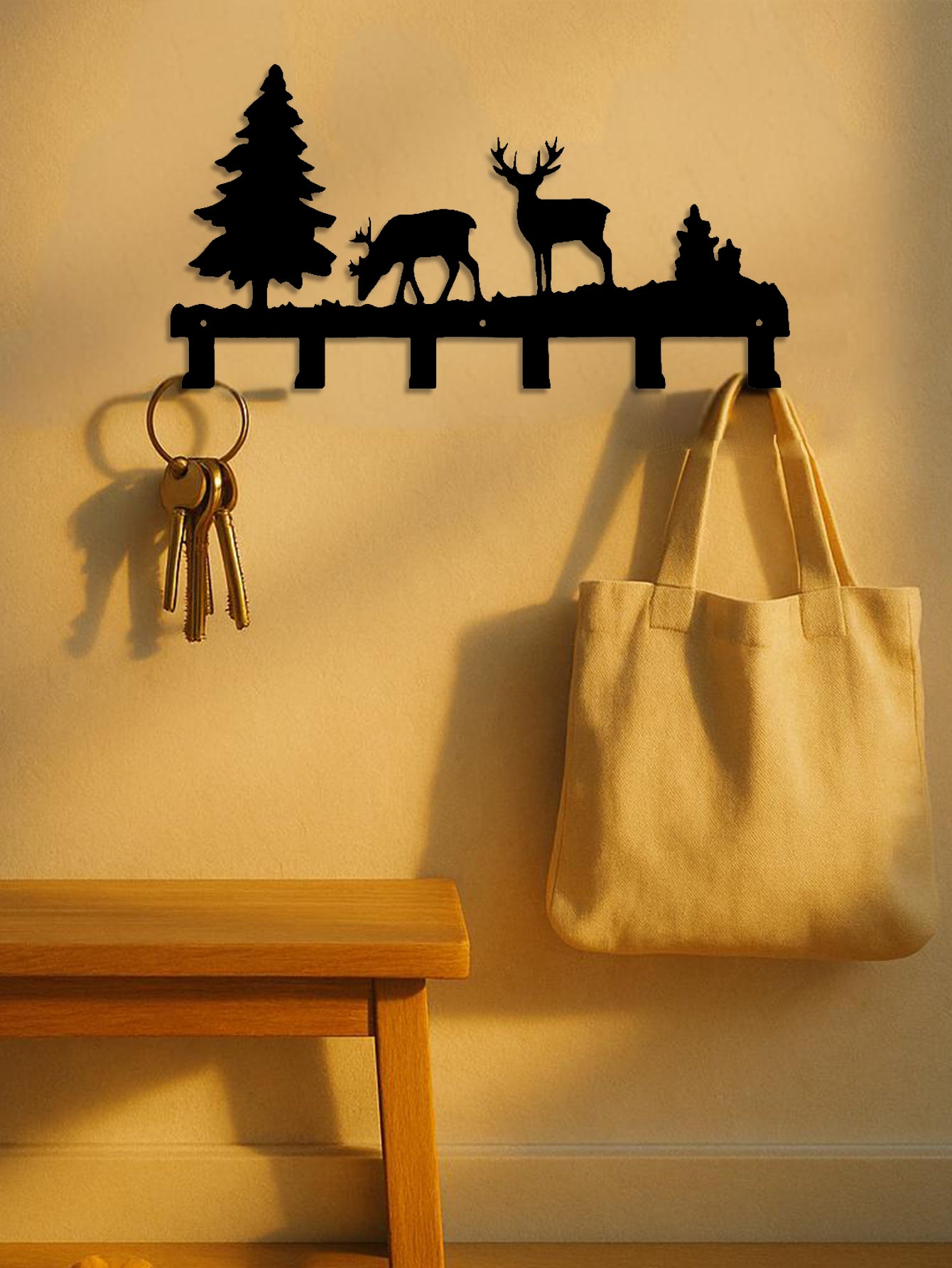 Decorative 6-hook wall mounted key and coat rack with deer and tree design, holding keys and a bag on a beige wall.