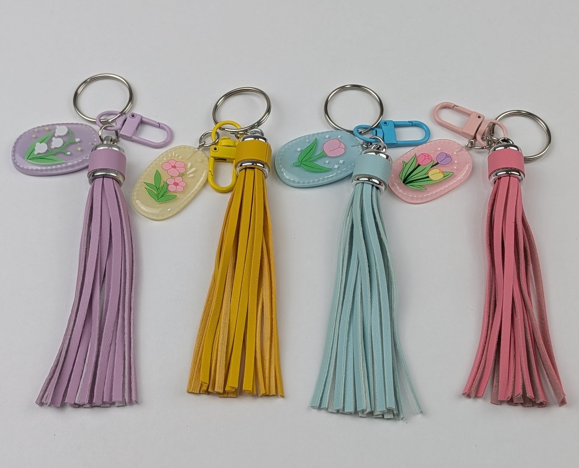 Four colorful faux leather tassel keychains on with raisin flower charm a light gray background. Buy online