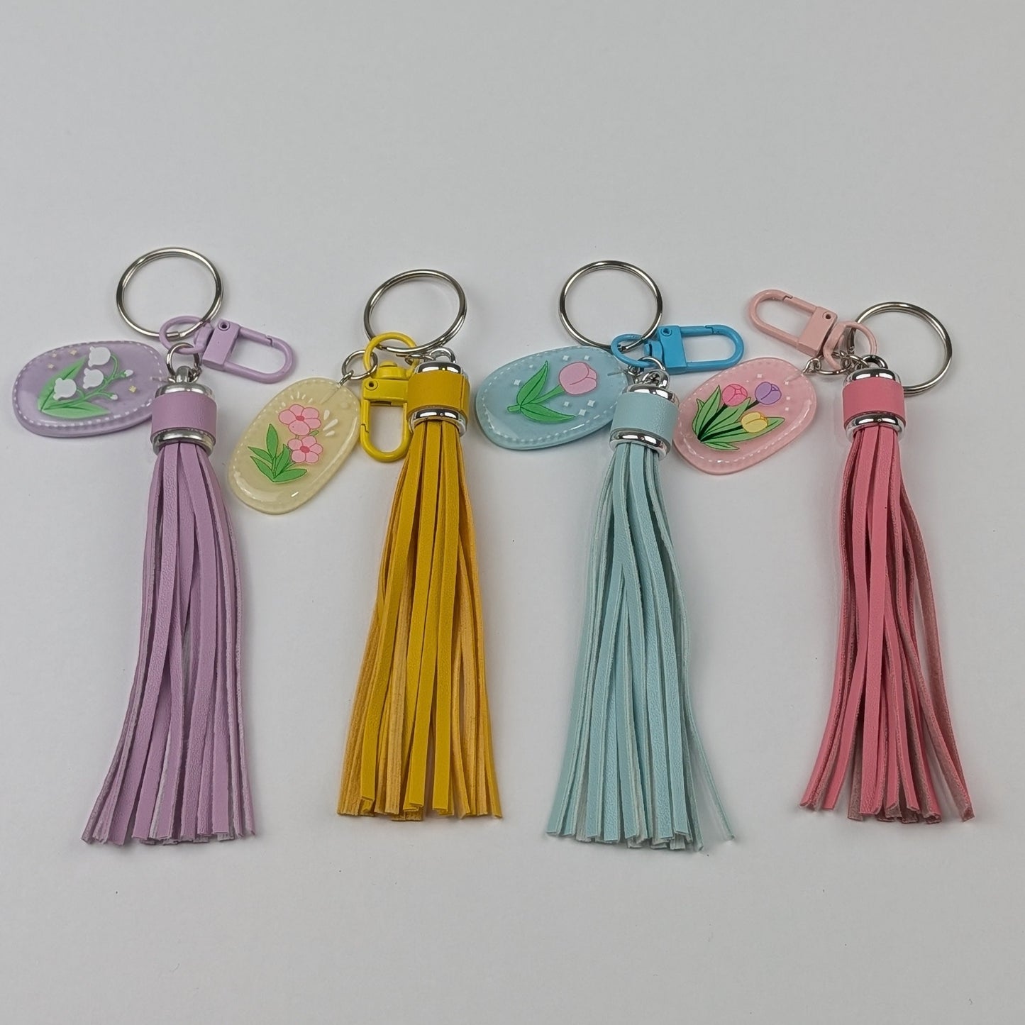 Four colorful faux leather tassel keychains on with raisin flower charm a light gray background