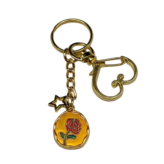 Golden hear shaped clasp keychain with a rose charm on a gray background