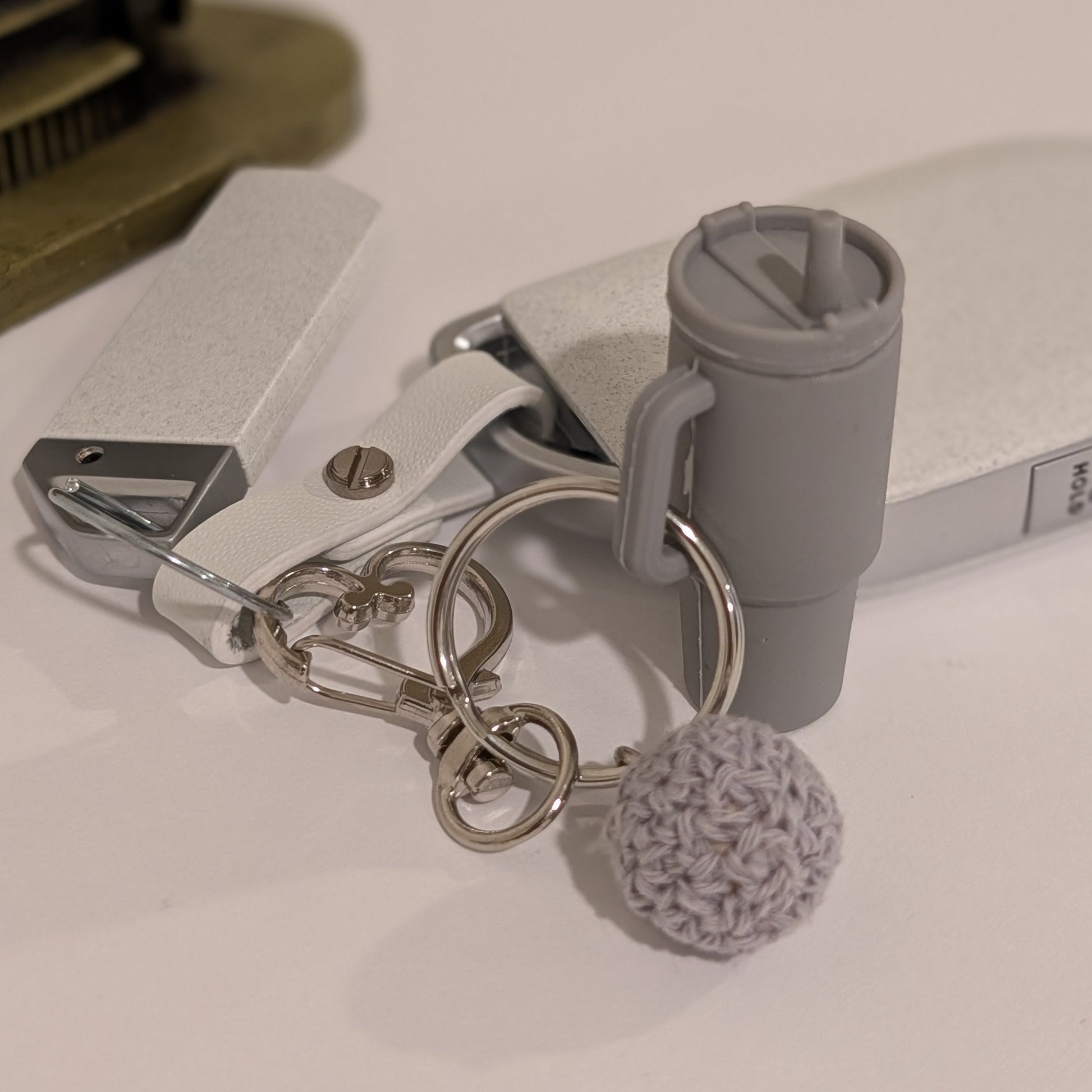 Gray silicone Keychain with black tumbler, white flower charm, and pom-pom attached to a car key on a light surface.