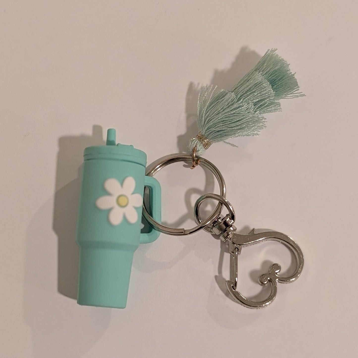 Green tumbler-shaped keychain with a tassel and heart shaped spring hook on a beige background