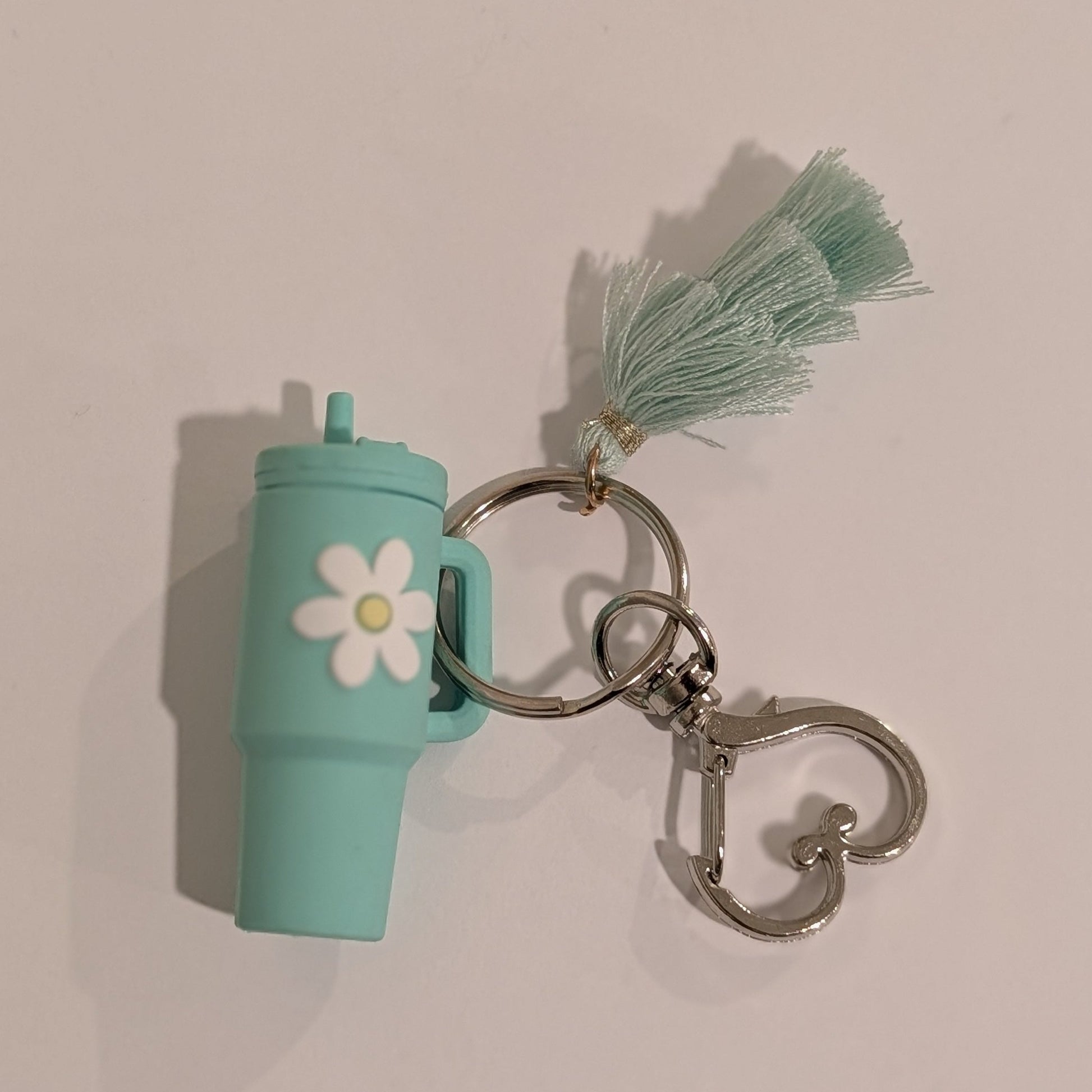 Green tumbler-shaped keychain with a tassel and heart shaped spring hook on a beige background