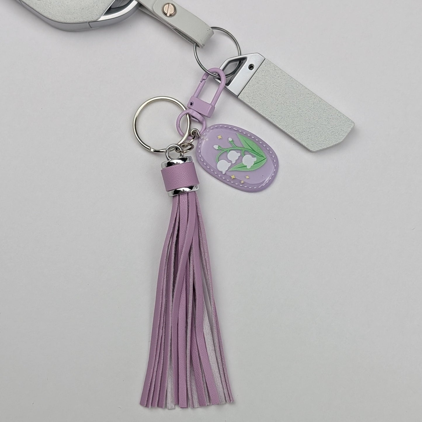 Keychain with purple faux leather tassel and floral tag attached with a car key on a light gray background