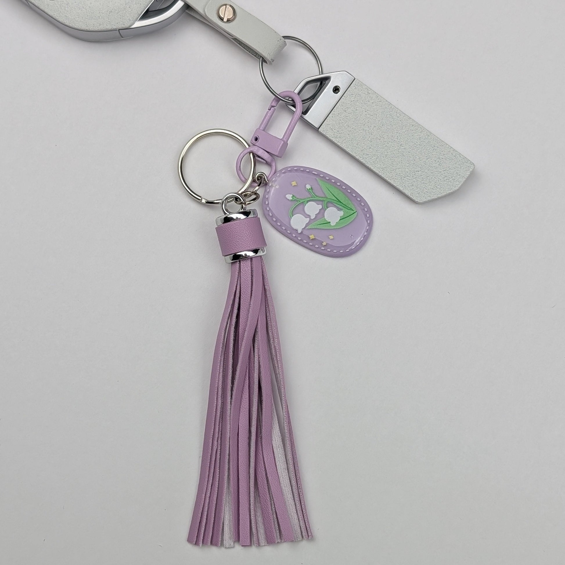 Keychain with purple faux leather tassel and floral tag attached with a car key on a light gray background