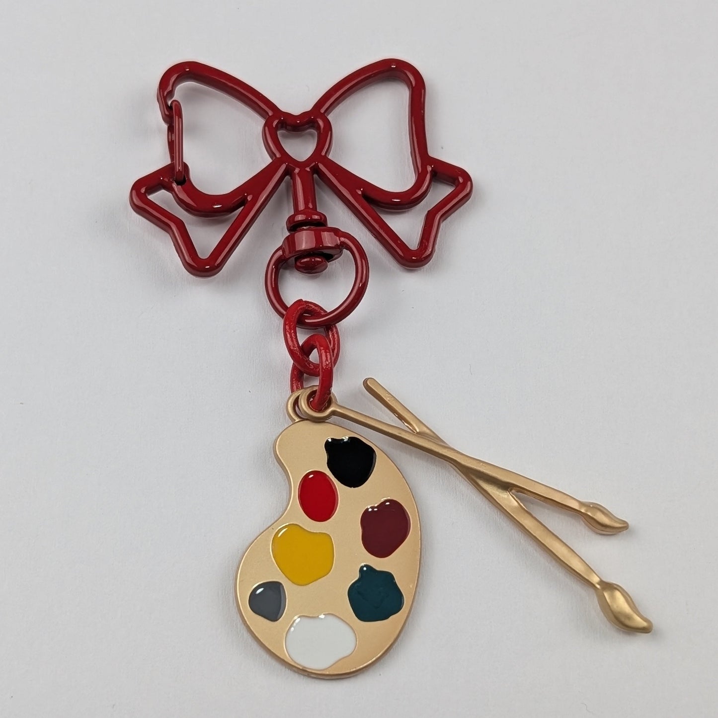 Keychain with red bow, paint palette, and brushes on a light gray background