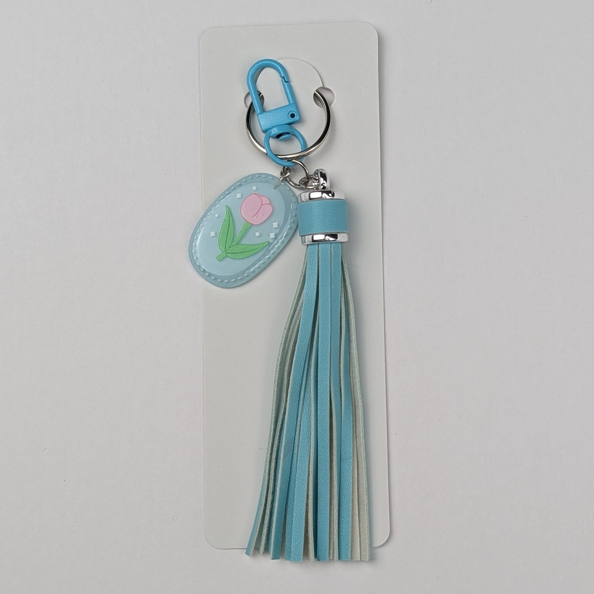 Keychain with teal tassel and floral charm attached to packing strip on a light gray background