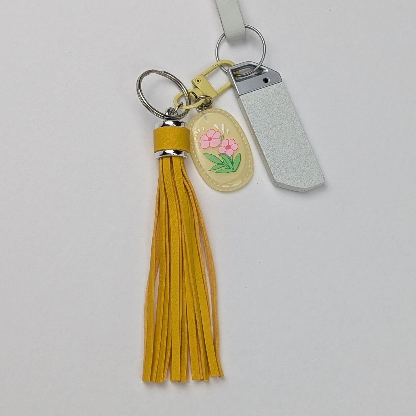 Keychain with yellow faux leather tassel and floral charm attached to a car key on a light gray background