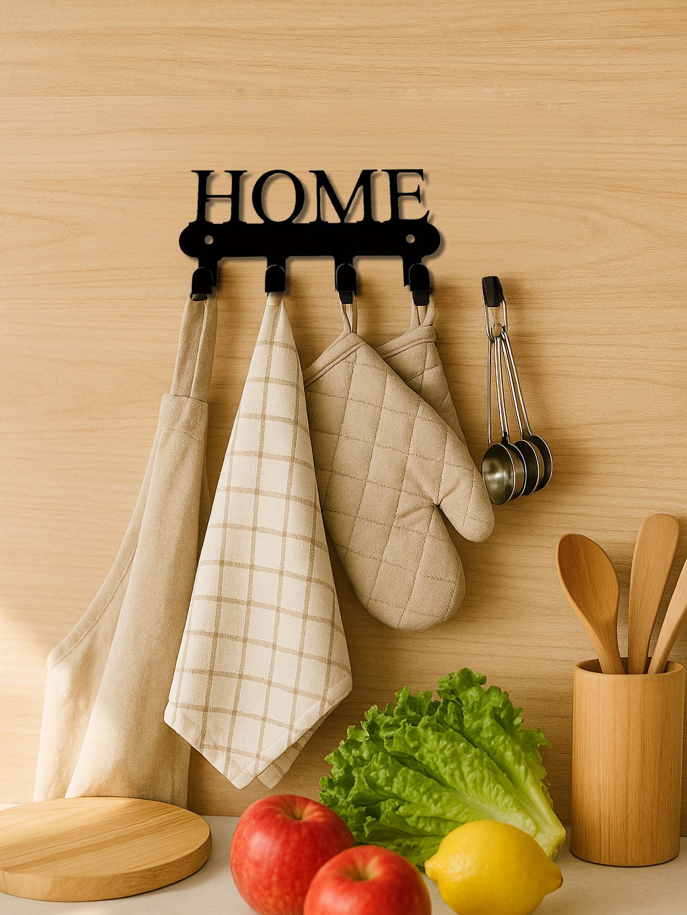 Kitchen wall with 4-hook wall mounted key and coat rack with 'HOME' text design holding kitchen items like towels, an oven mitt, and measuring cups.