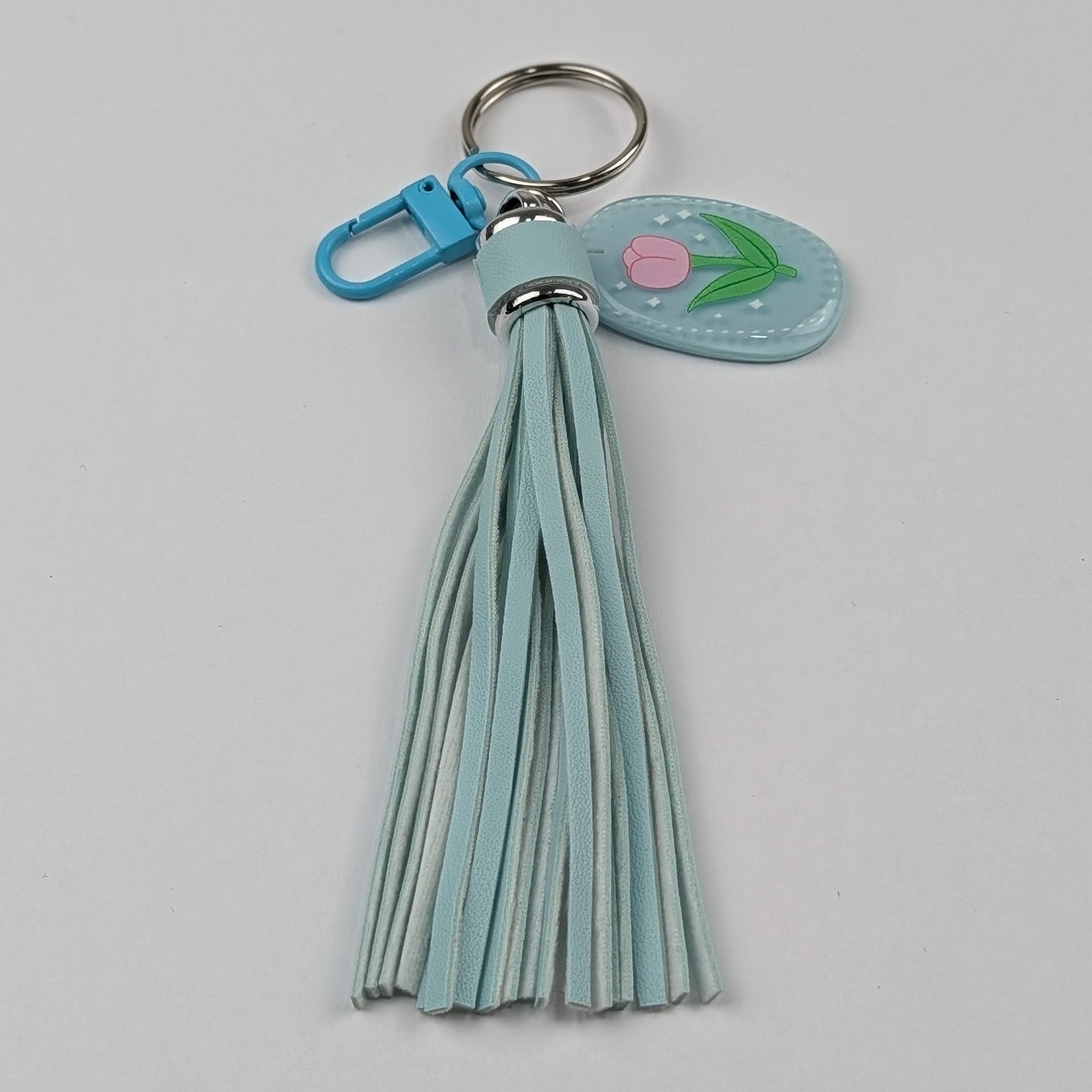 Light blue faux leather tassel keychain with a floral raisin charm on a light gray background