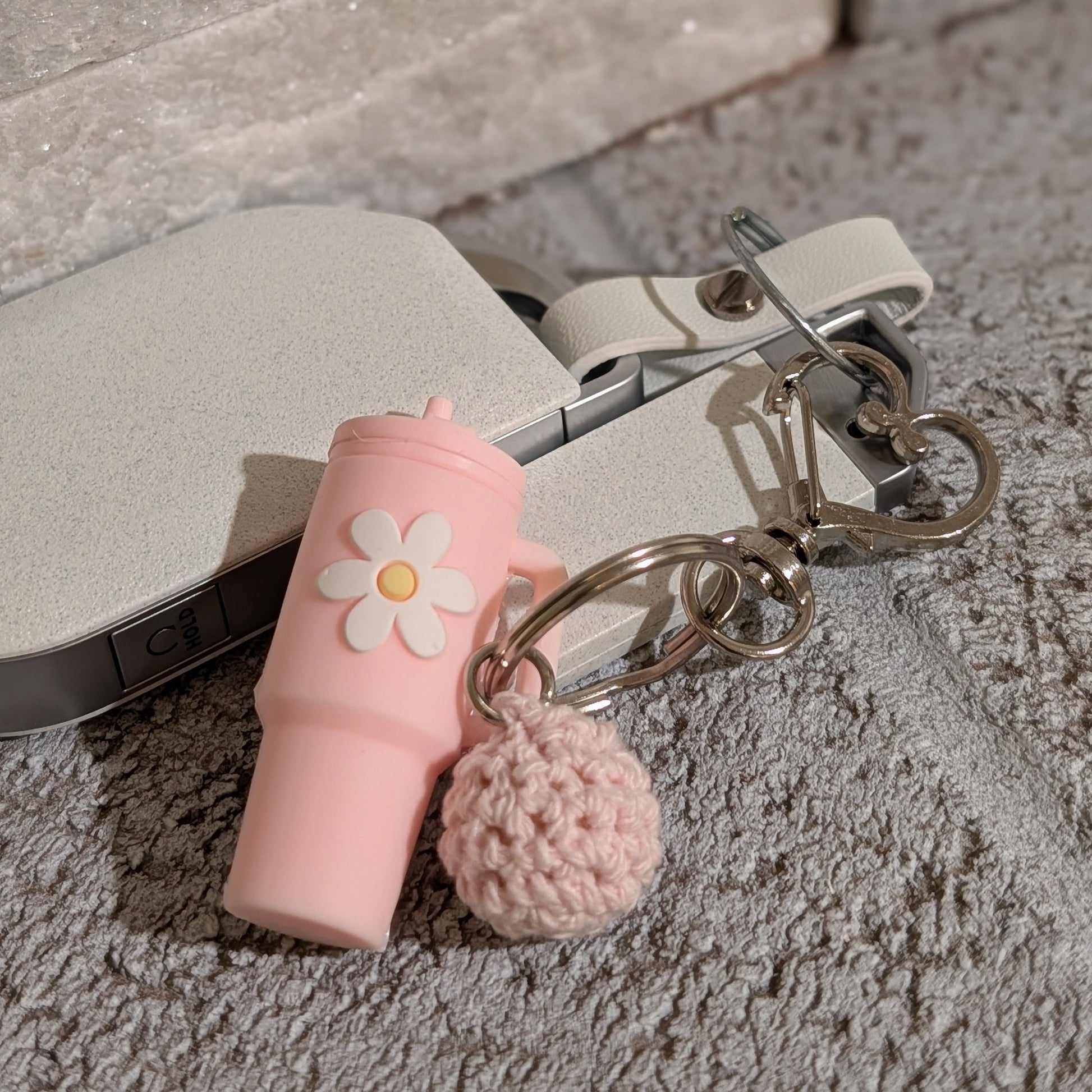 Light pink silicone tumbler key chain with crochet ball and heart shaped hook attached to a car key on a gray surface