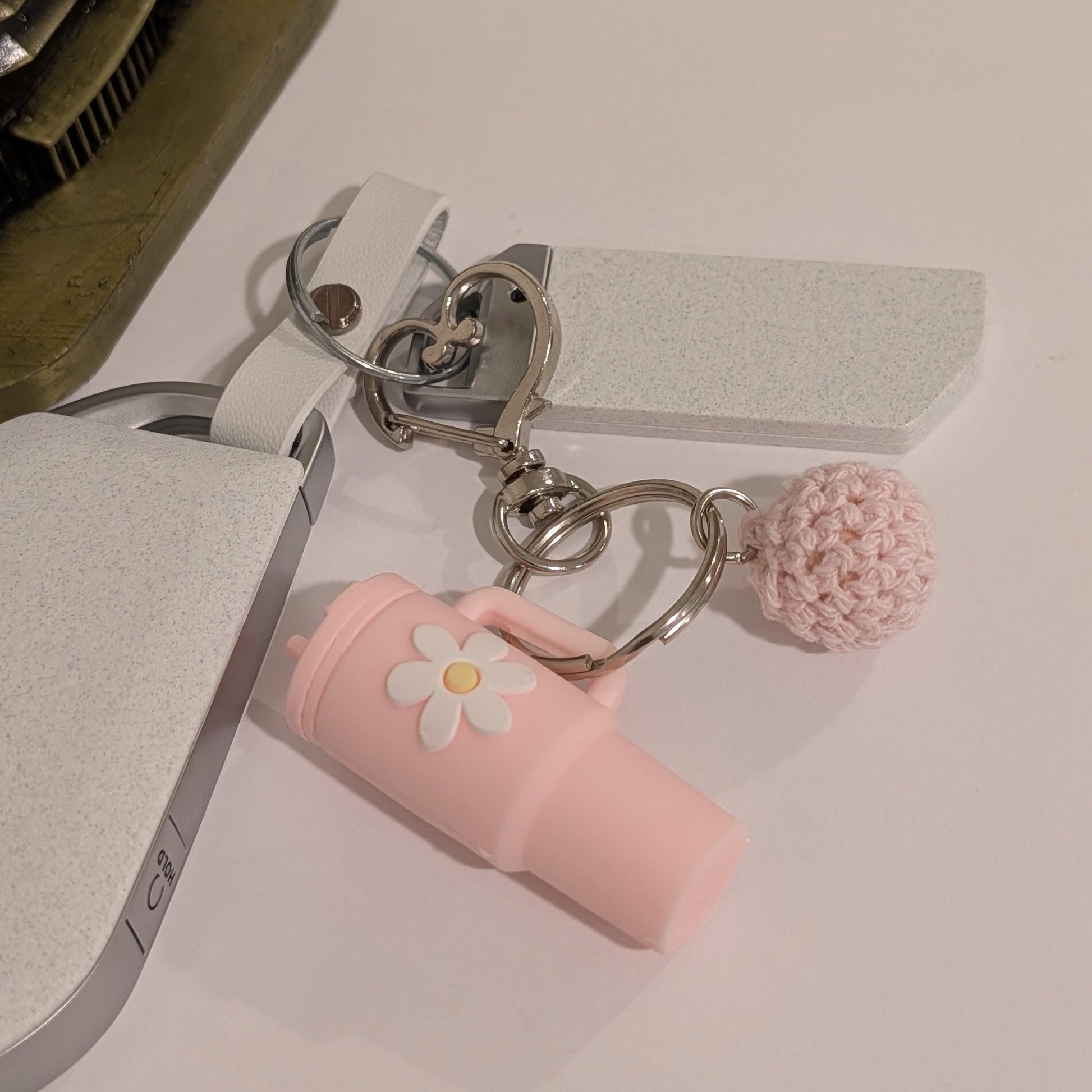 Light pink silicone tumbler key chain with crochet ball and heart shaped hook attached to a car key on a white surface next to an ornament