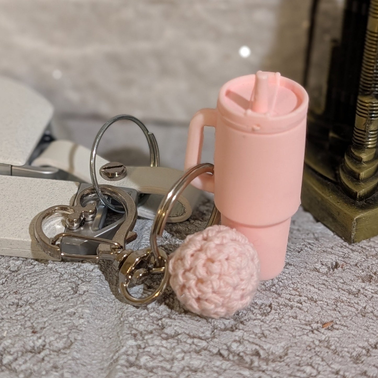 Light pink silicone tumbler key chain with crochet ball and heart shaped hook on a gray surface
