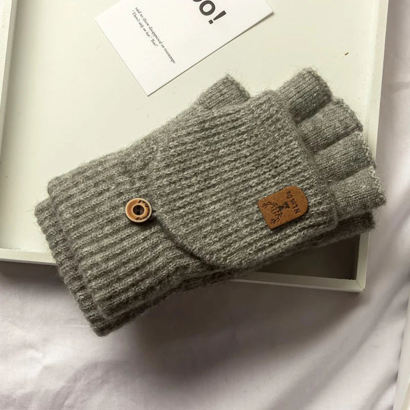 Pair of gray knitted fingerless gloves with a brown button and label on a light background