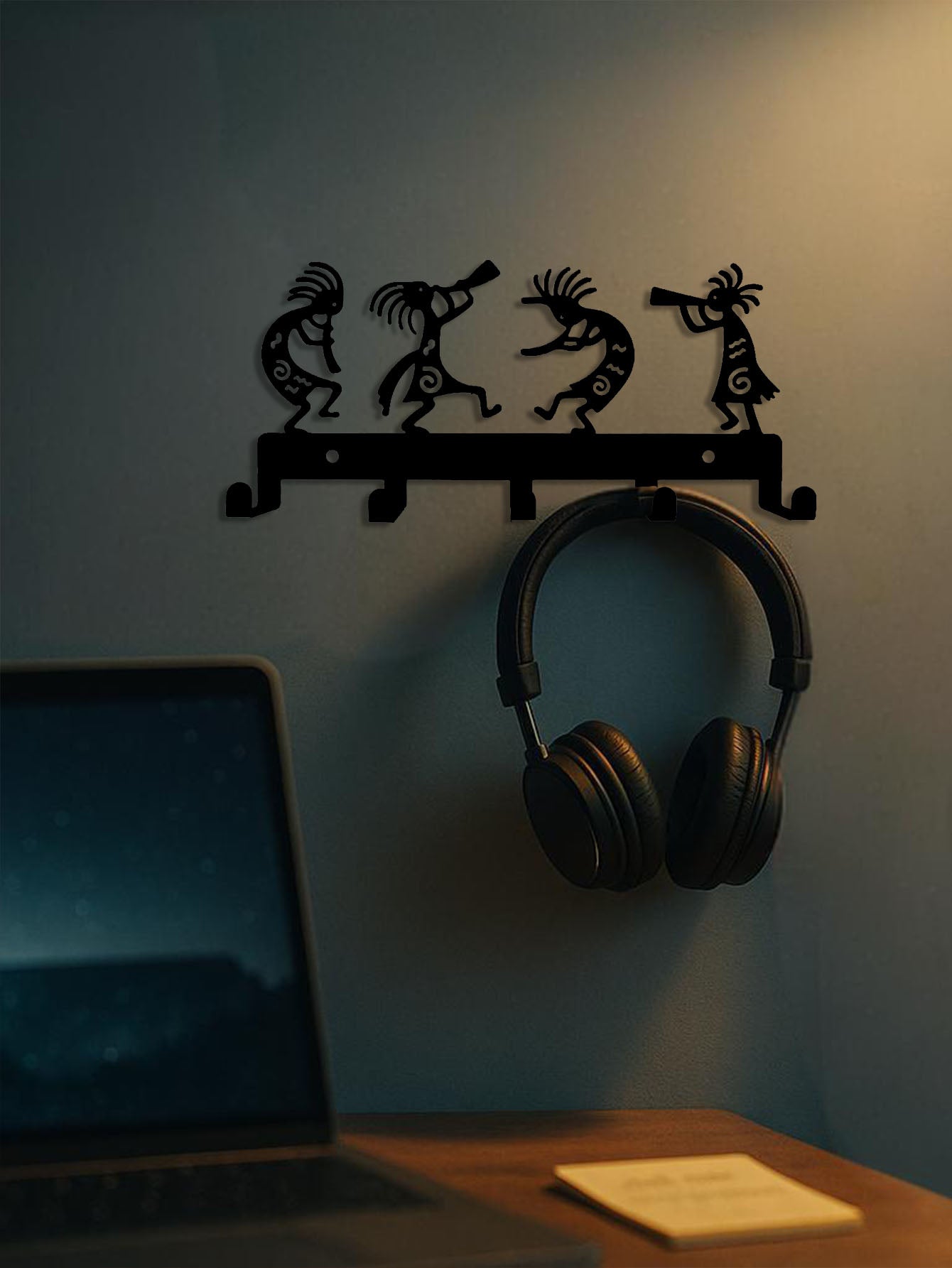 Pair of headphones hanging on a wall hook with decorative figures above a laptop on a desk.