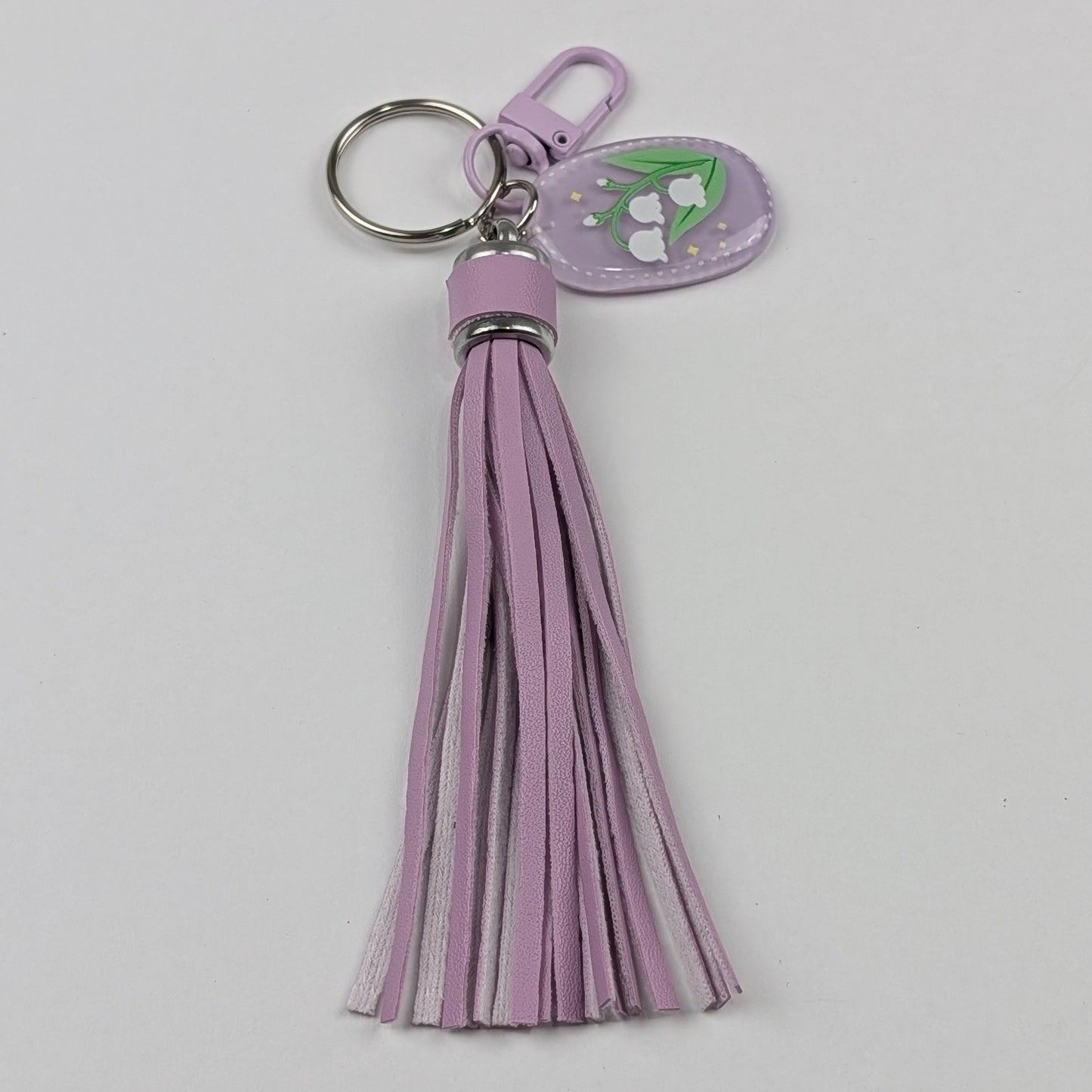 Purple faux leather tassel keychain with a floral raisin charm on a light gray background