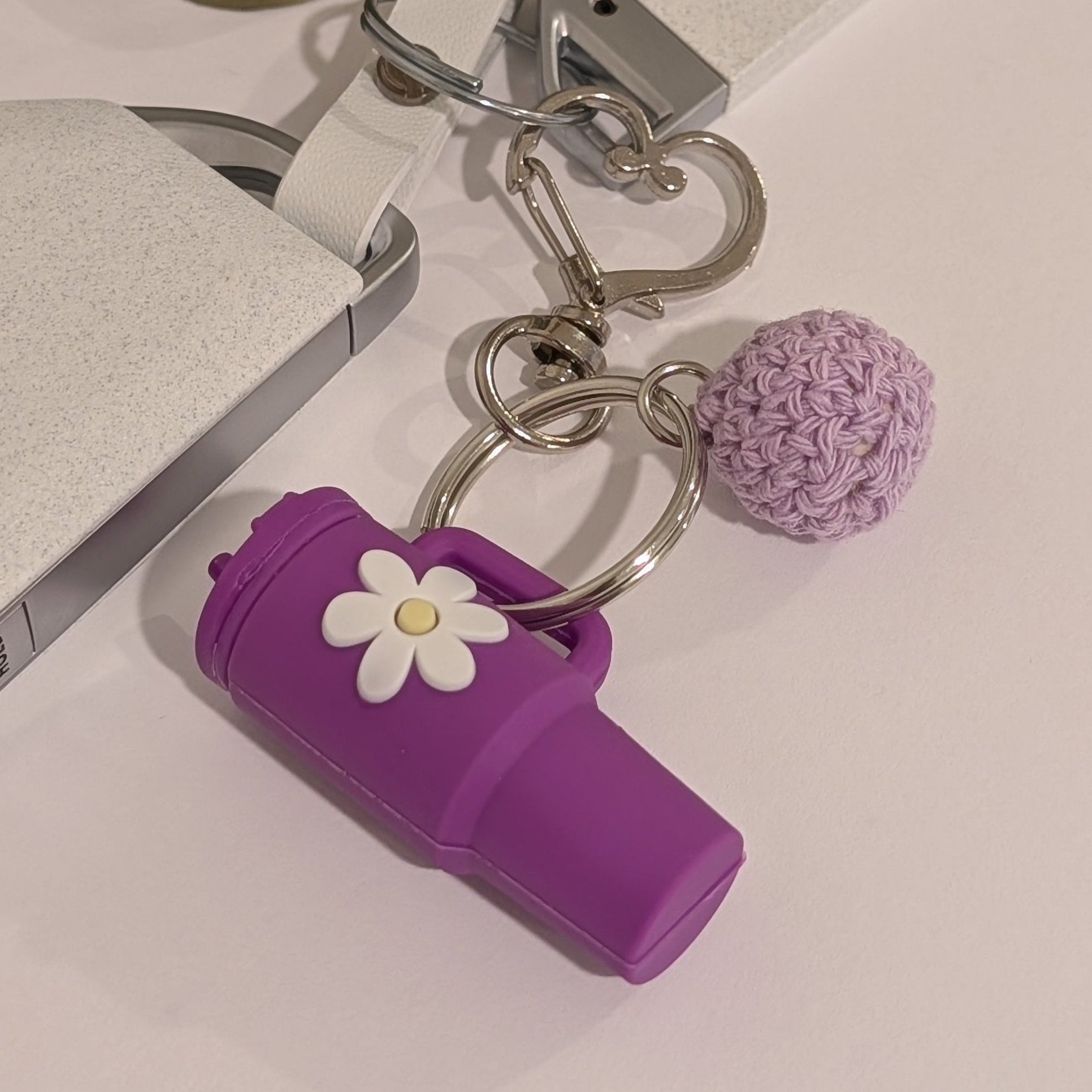 Purple silicone Keychain with black tumbler, flower charm, and pom-pom on a light surface.