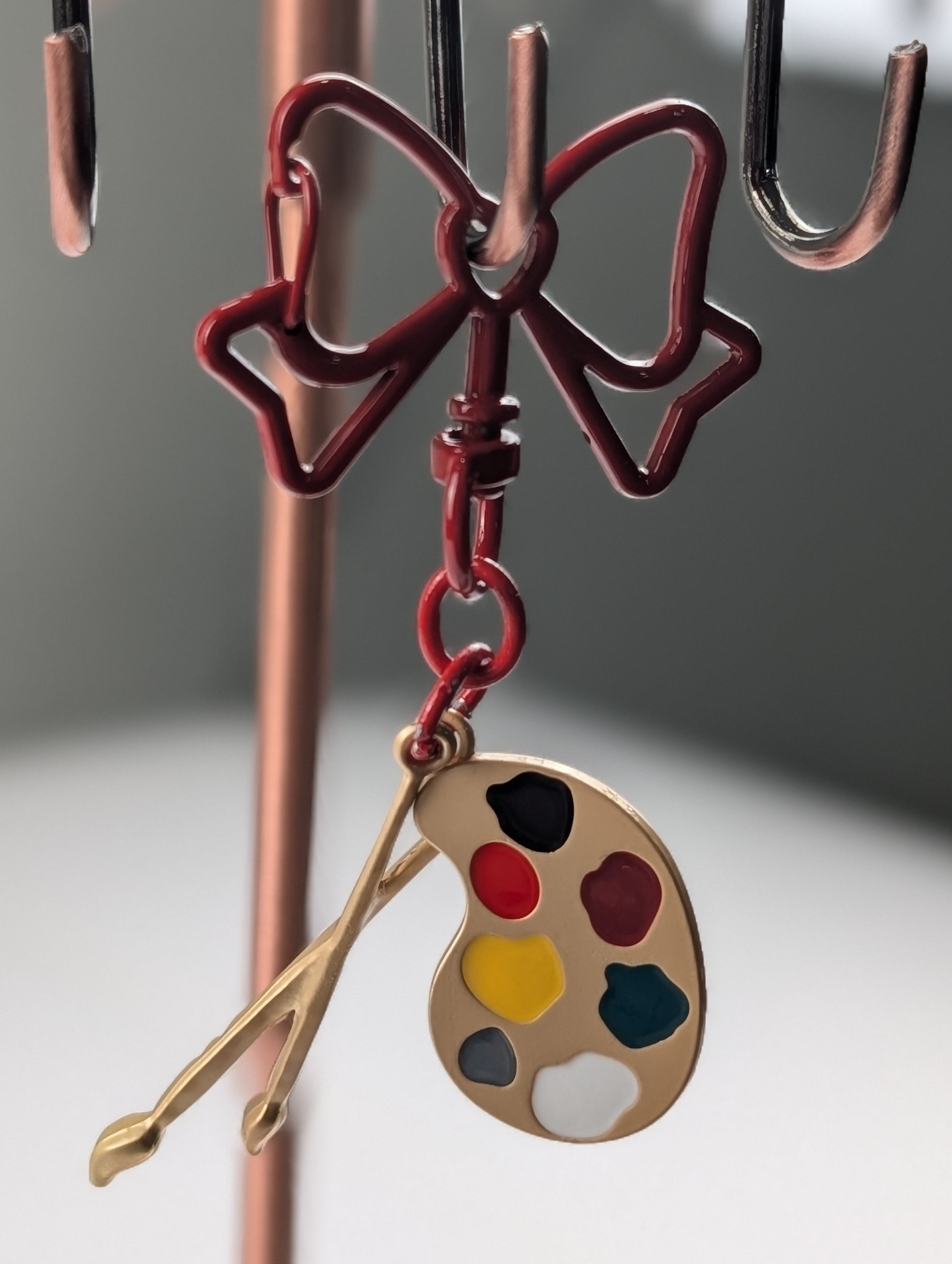 Red bow hook keychain with a paint palette charm on a gray background