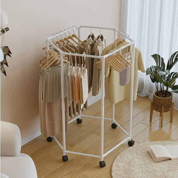 White hexagonal clothing rack with clothes on wheels in a room with a plant and rug.