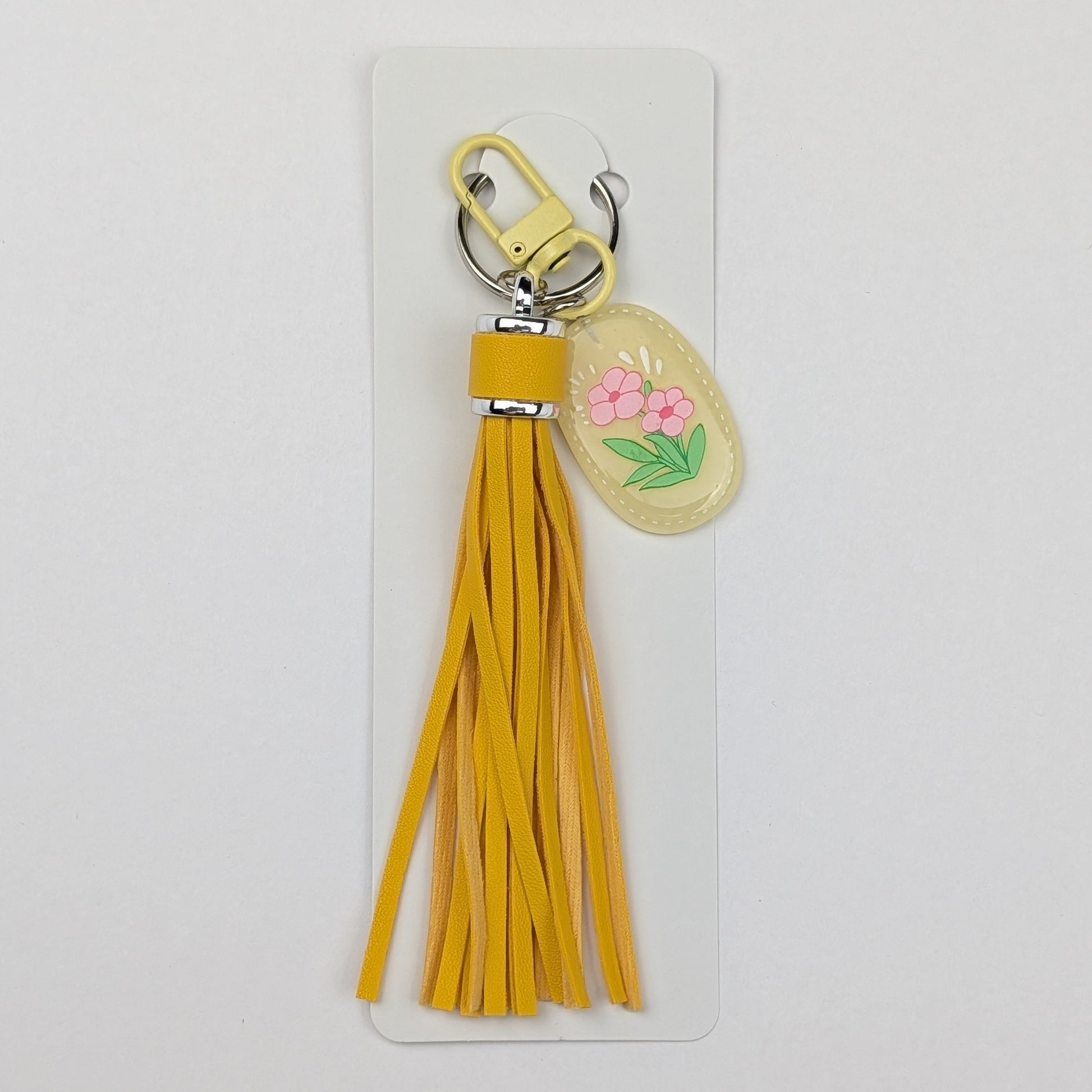Yellow tassel keychain with floral design attached with a white packaging card on a white background