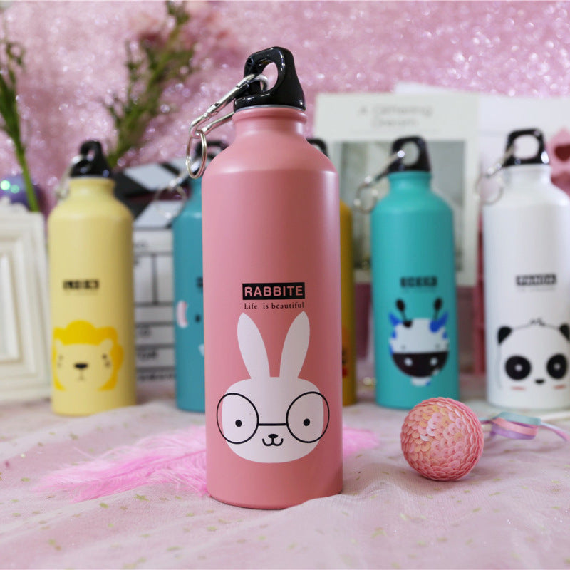 Image for stainless steel reusable water bottle for kids in pink color with rabbit face print on it. It has "RABBIT" text right above the face and a "Life is beautiful" quote right below it. The bottle is shown standing straight with a small decoration ball lying next to it and few other similar bottles in the background.