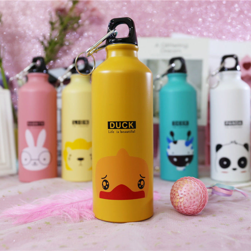 Image for stainless steel reusable water bottle for kids in yellow color with duckling face print on it. It has "DUCK" text right above the face and a "Life is beautiful" quote right below it. The bottle is shown standing straight with a small decoration ball lying next to it and few other similar bottles in the background.