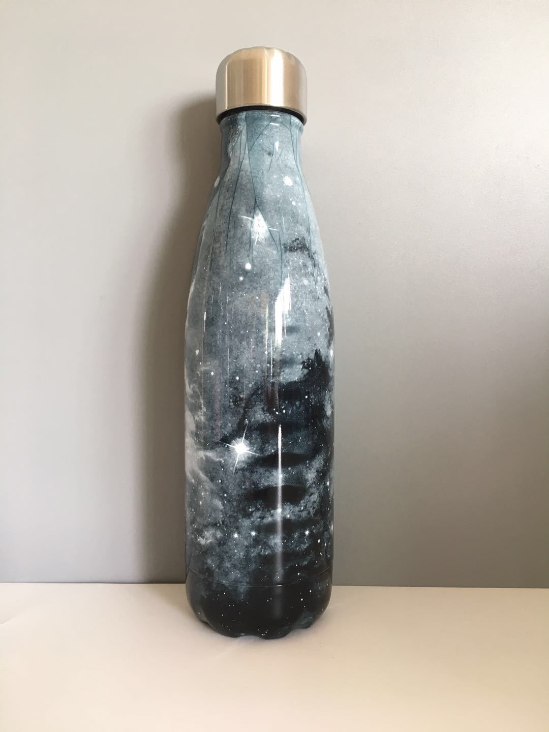 Image for stainless steel vacuum flask with sky galaxy style printing in grey color shade. The bottle has a stainless steel cap with a silicone sealing ring inside to keep it air tight when capped.
