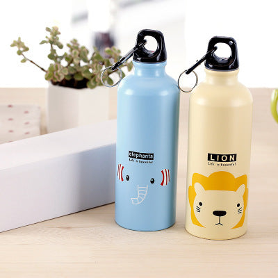 Image for two reusable stainless steel water bottles for kids lying straight next to each other, one in blue color with elephant face and the other in light yellow color with lion face printed on it. There are green decorative leaves in a white holder cup in the background.