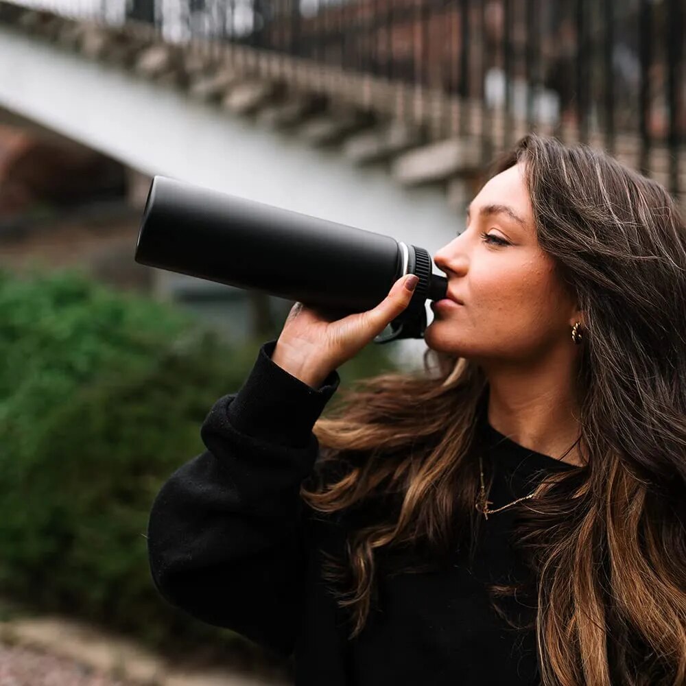 Image for a woman sipping form the 32 oz black stainless steel water bottle with double wall vacuum insulation.