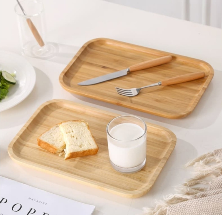 Image with two bamboo serving trays, one with cutlery in it and another one with a milk up and two pieces of bread.
