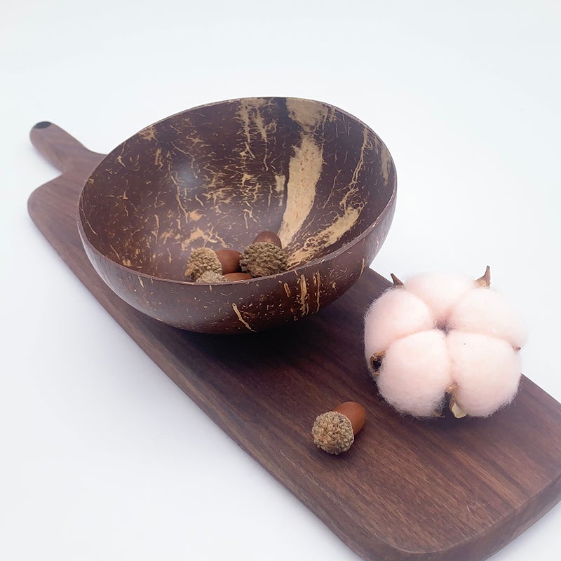Image for a coconut bowl with some dried flowers in it, placed on a wooden cutting board and a small cotton plush next to it.
