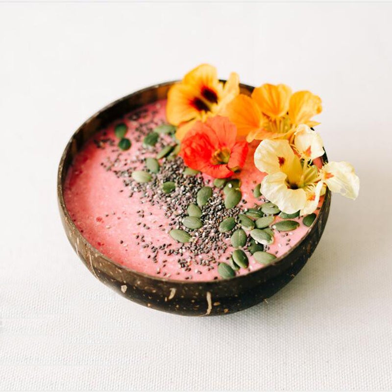 Coconut bowl filled with pink color dessert decorated with flowers.