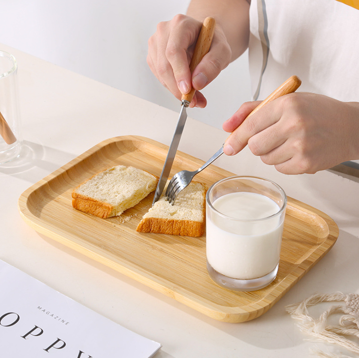 Image with person eating the bread from bamboo serving tray using fork and knife. A milk cup is also placed in the tray.