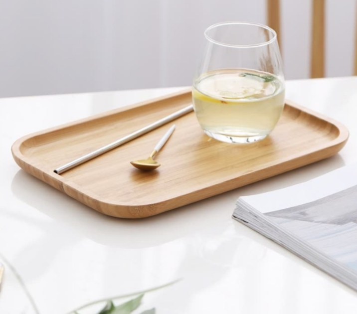 Image with bamboo serving tray containing a cup with drink in it. A spoon and a drinking straw is placed in tray next to the drink.
