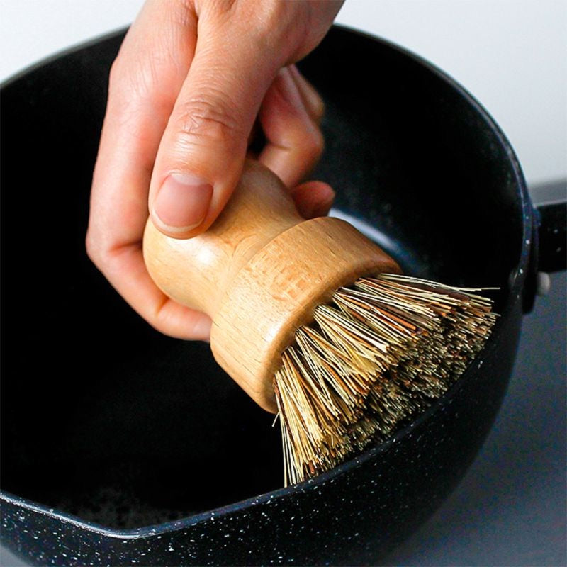 Image for a small bamboo bowl brush with brown bristles being used to clean a black frying pan.