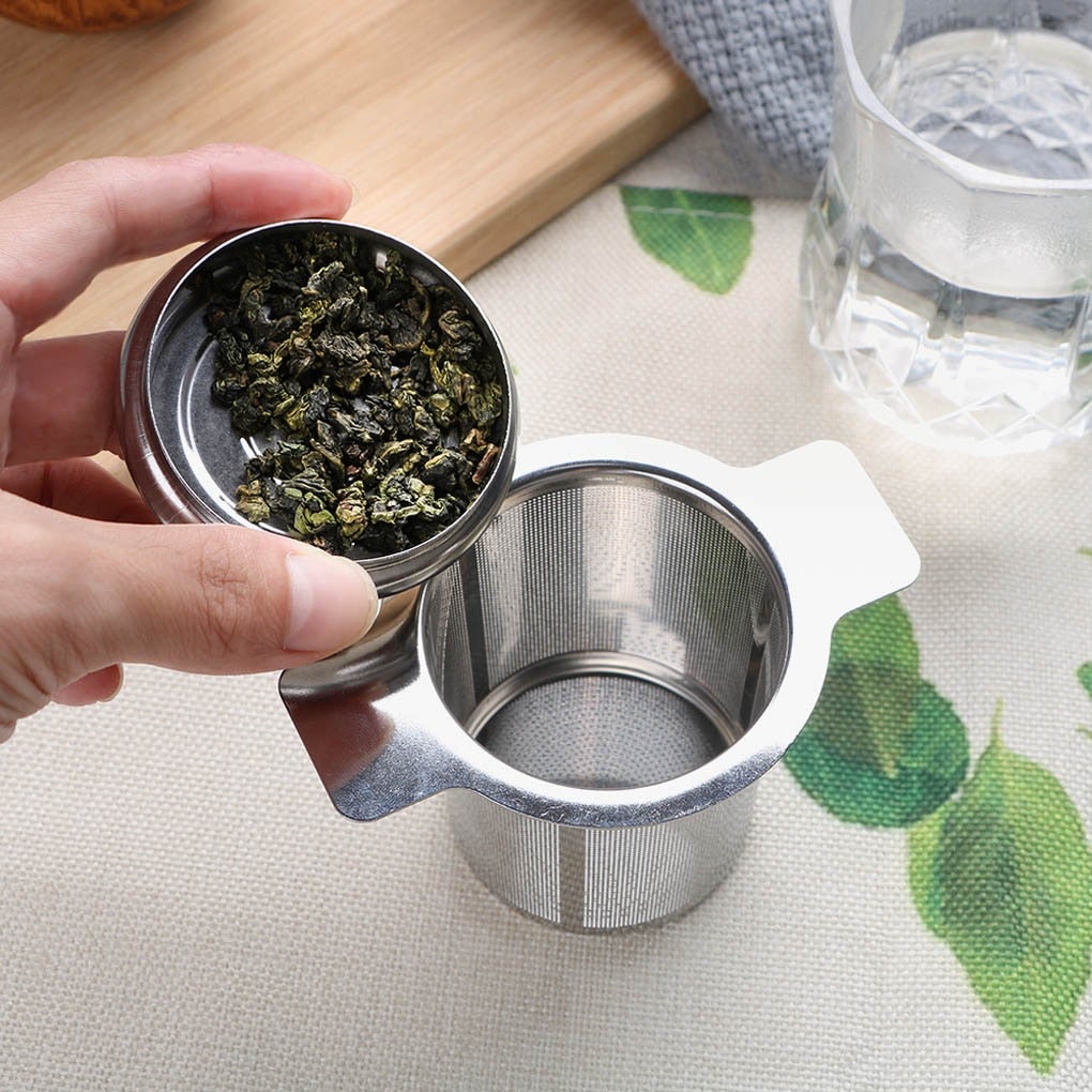 Image for stainless steel loose leaf tea infuser and its lid. The lid is filled with dry tea leaves.