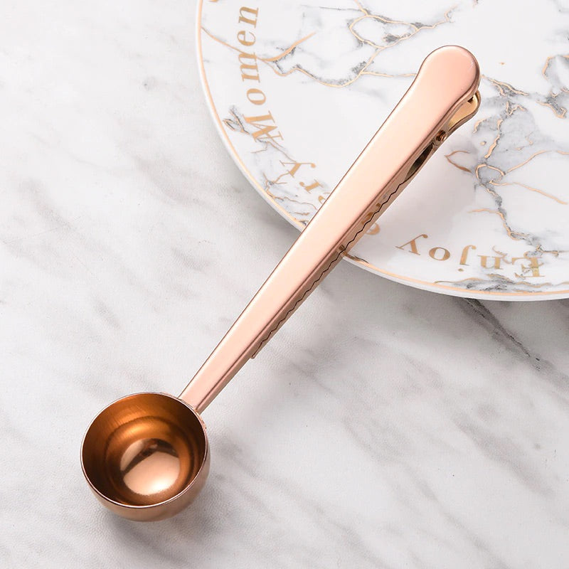Image for rose gold color two-in-one stainless steel spoon and sealer placed on a plate.