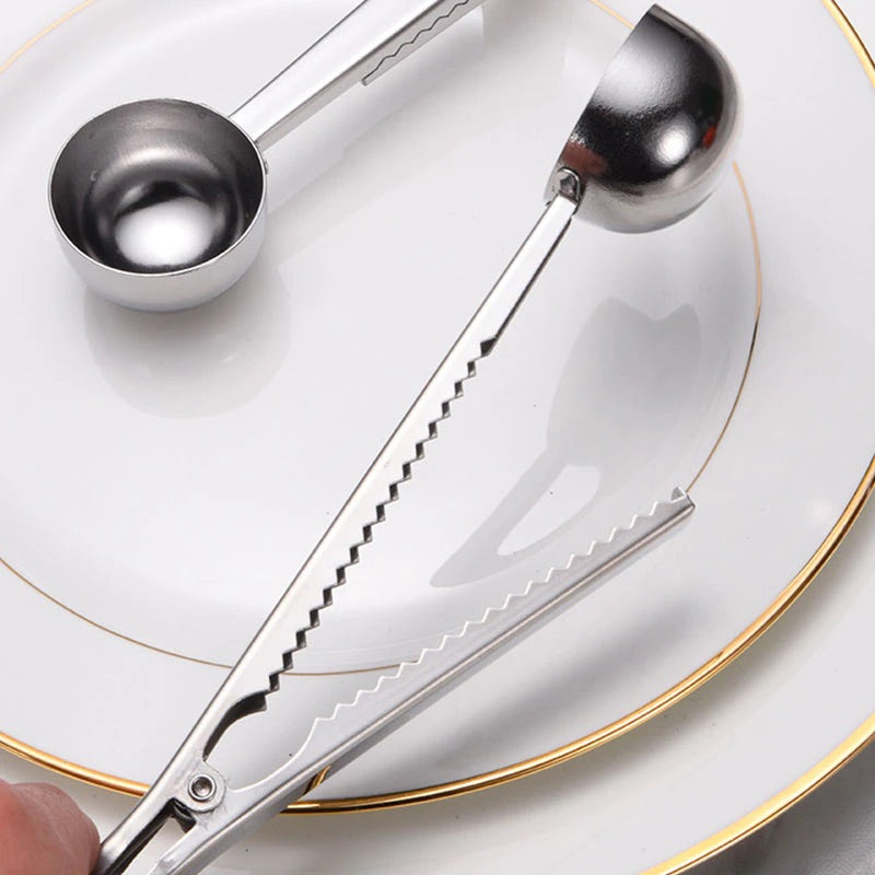 Image for silver color two-in-one stainless steel spoon and sealer placed on a plate with the clip being opened. The clip is built into the handle.